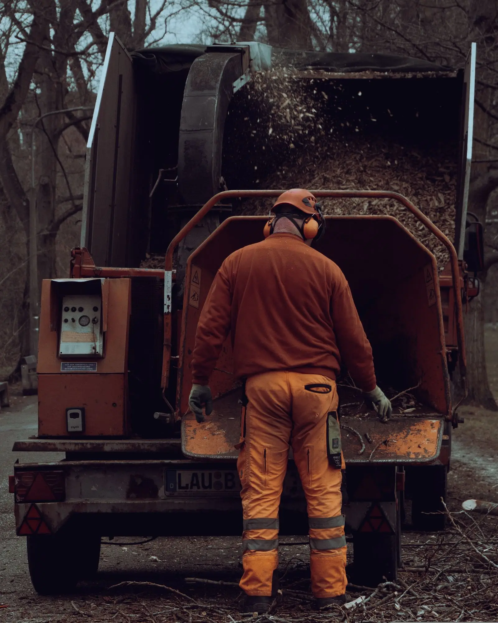 Worker in ear protection standing at the back of a wood chipper