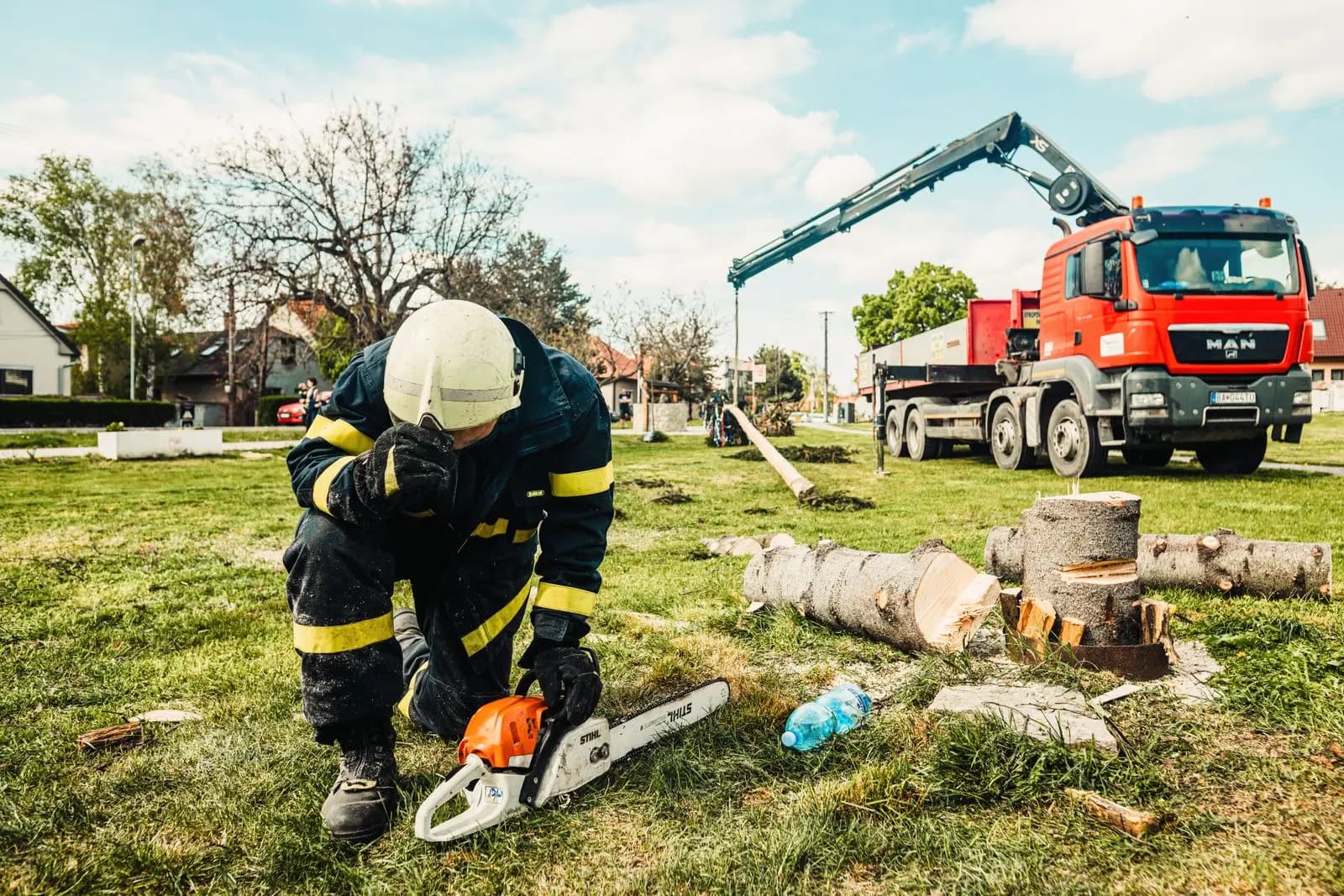Chainsaw operator beside cut log sections with a crane truck in the background