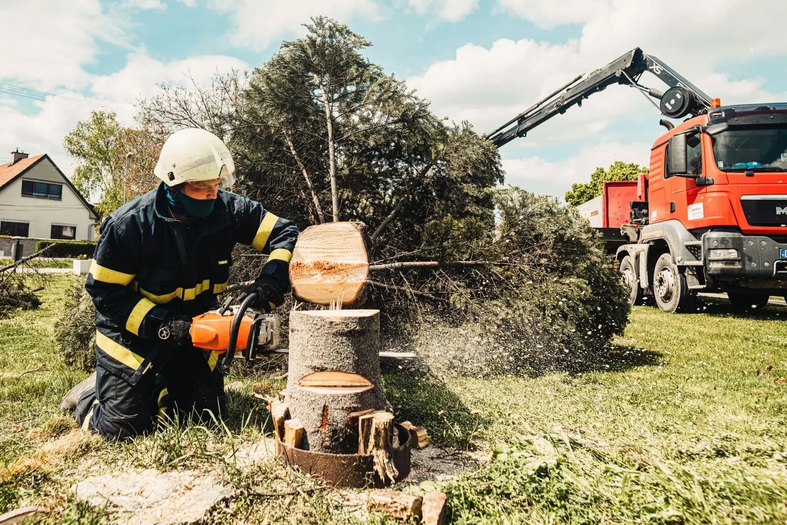 Worker cutting a trunk section on the ground with a crane truck behind