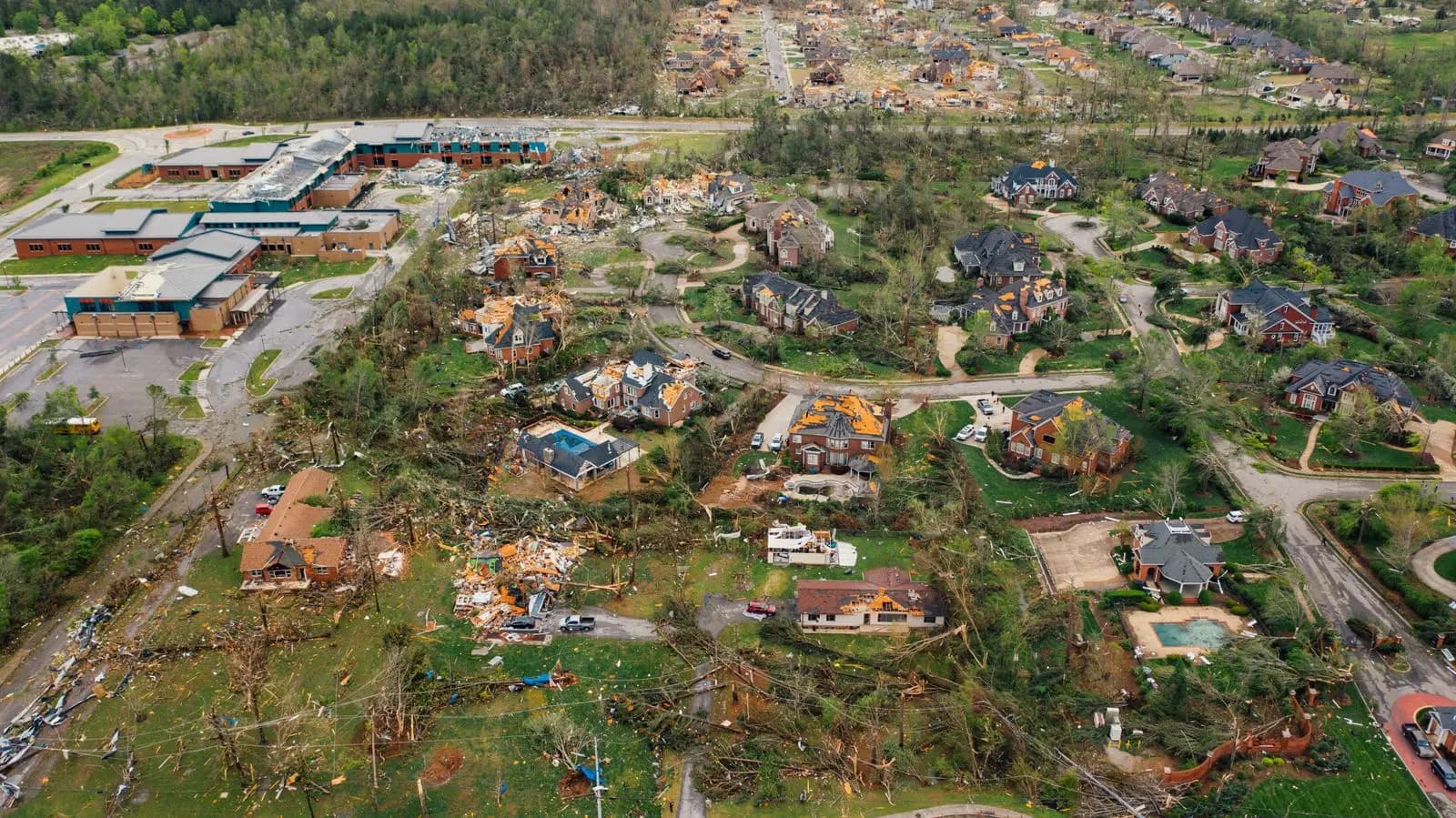 Aerial view of a neighborhood with damaged roofs and downed trees after a tornado